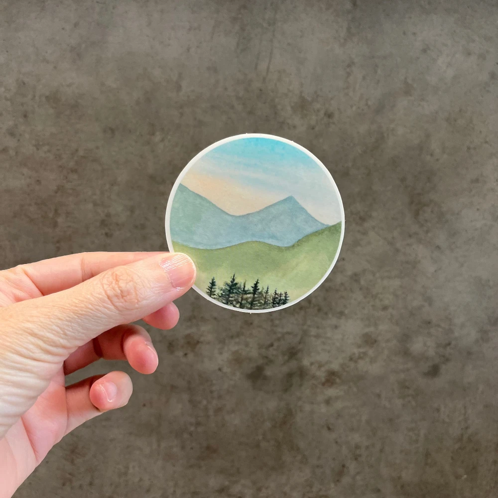 Watercolor mountain landscape vinyl sticker held in hand