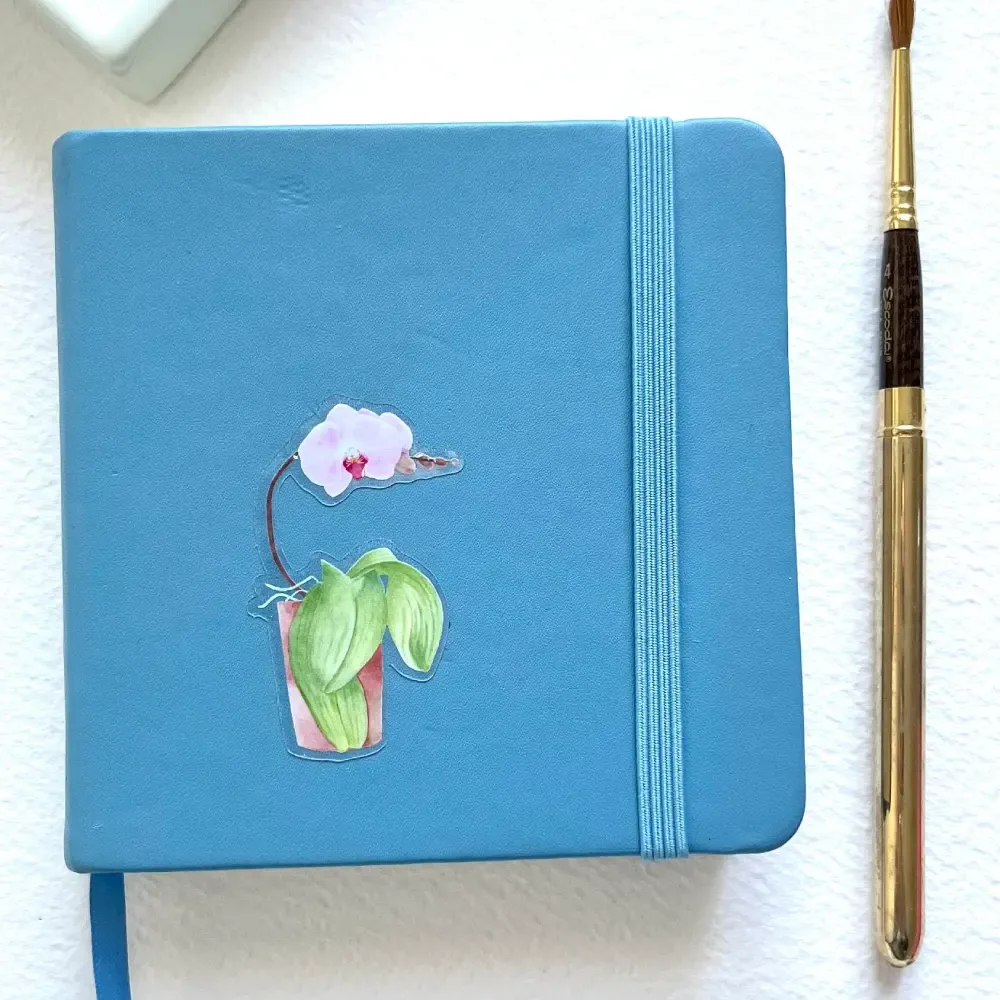 Watercolor orchid vinyl sticker on notebook